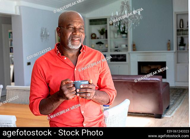 Thoughtful african american senior man looking away while having coffee at home