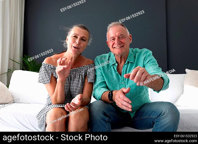 Happy caucasian senior couple in living room, on couch making video call, gesturing and smiling