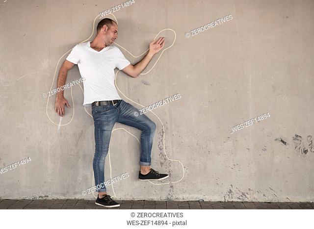 Man pretending to be dead standing with chalk outline drawn on concrete wall