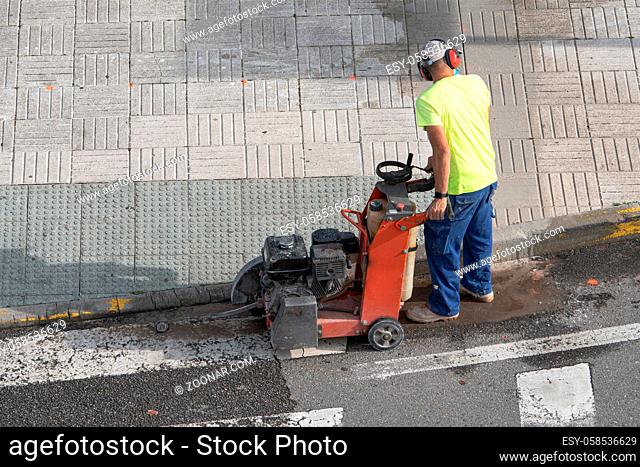 Construction worker cutting concrete floor with diamond saw blade machine on a sidewalk