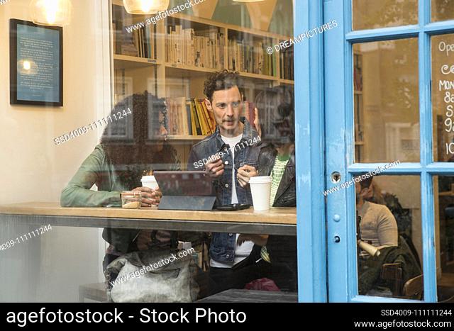 Group of friends sitting in window of cafe with tablet