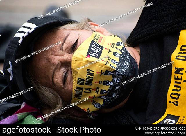 A mother of a relative killed during the flase positives lays on the ground with a shirt and a face mask that reads ""Who gave the order?"" with photos of army...