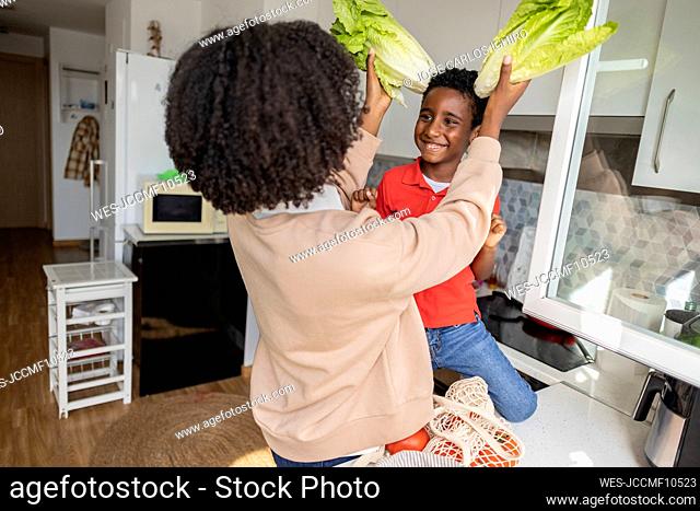 Playful mother holding lettuce on son's head in kitchen at home