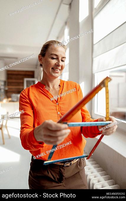 Smiling businesswoman making house shape with ruler in office