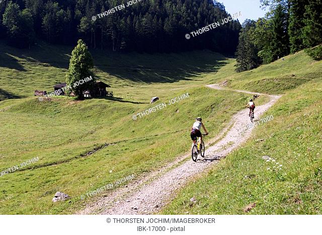 Two mountainbking girls on a flat gravel road on a summery open alpine country side in the region Wilder Kaiser in Austria
