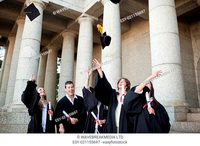 Graduates throwing their hats in the sky in front of their university