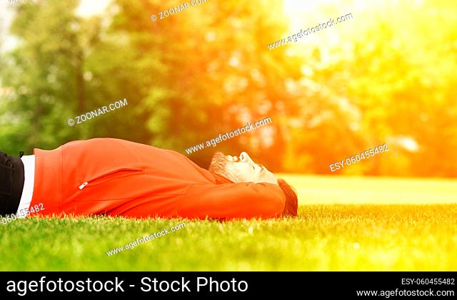 Handsome sport man training in park. Athlete in red jacket lying on green grass and doing trunk curls. Fitness and lifestyle concepts. Toned