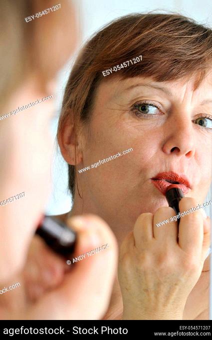 Head portrait in the mirror of a middle-aged brunette woman in front of the mirror with lipstick put on her lips