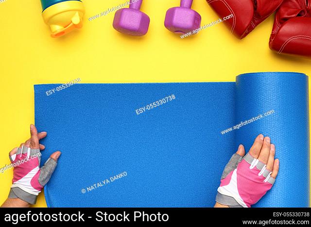 female hands in sports gloves unfold a sports mat on a yellow background, top view
