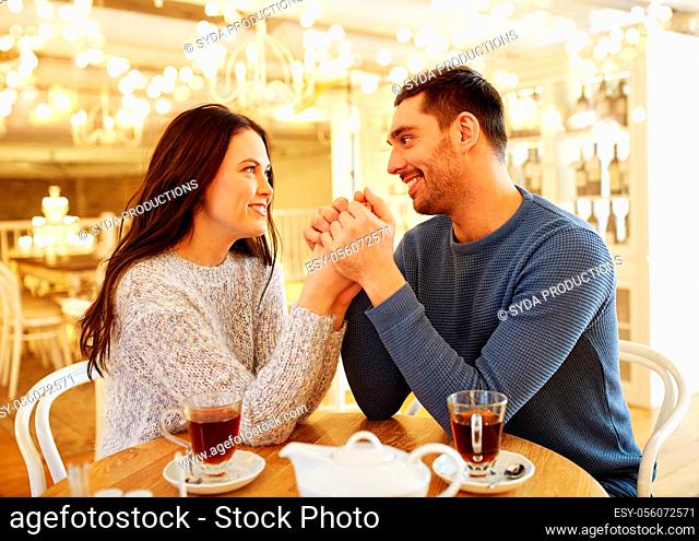 happy couple with tea holding hands at restaurant