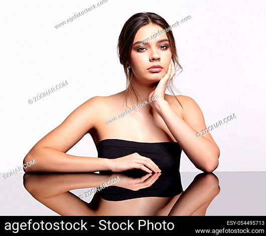Portrait of young beautiful woman. Female at reflecting table on gray background