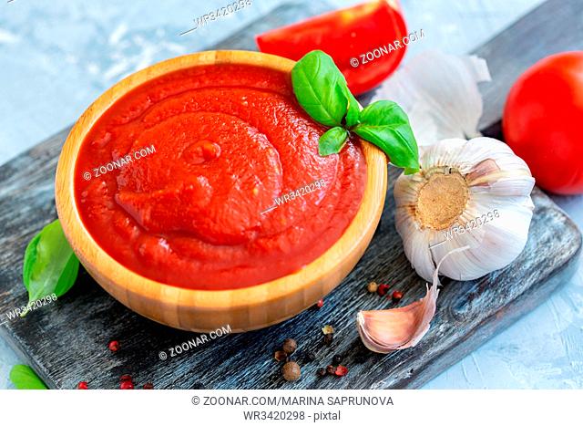 Spicy tomato sauce and green basil in wooden bowl, garlic and fresh tomatoes on grey concrete background, selective focus