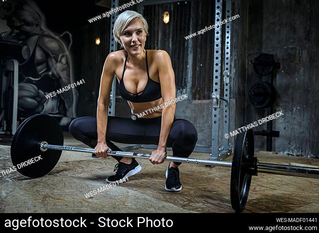 Blond sportswoman with barbell in gym