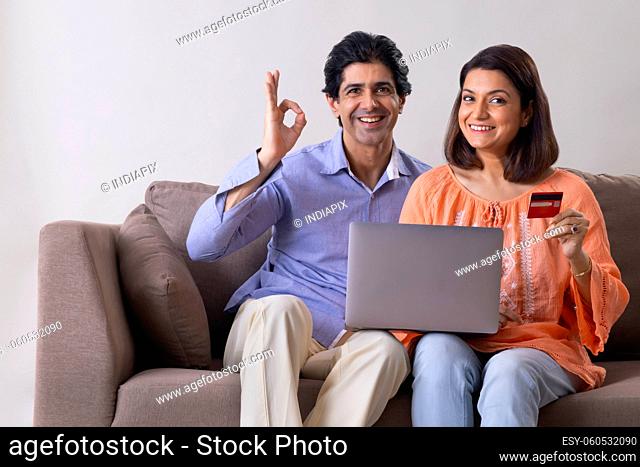 Happy Indian middle age couple posing together in front of camera during online shopping