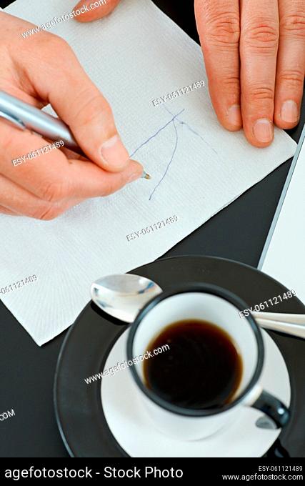Hands of businessman drawing graph on paper napkin with pen, beside a cup of coffee on table