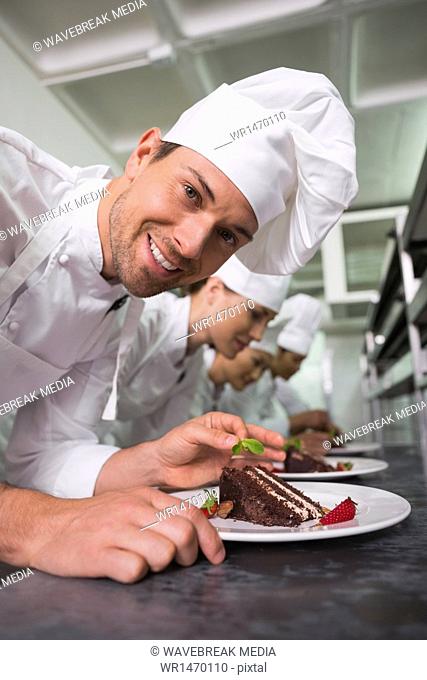 Row of chefs garnishing dessert with one smiling at camera