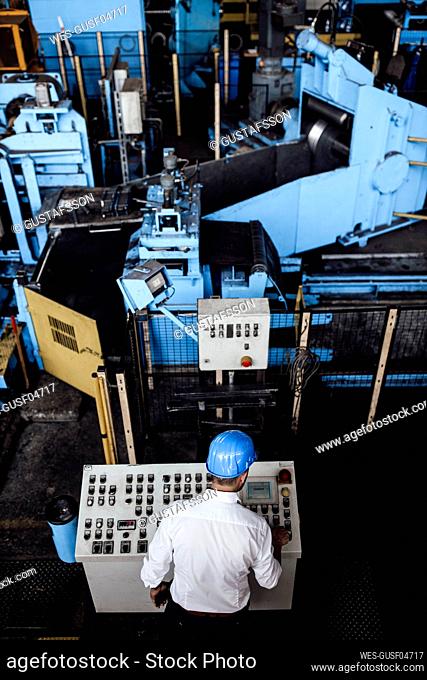 Male entrepreneur operating control panel while standing at factory