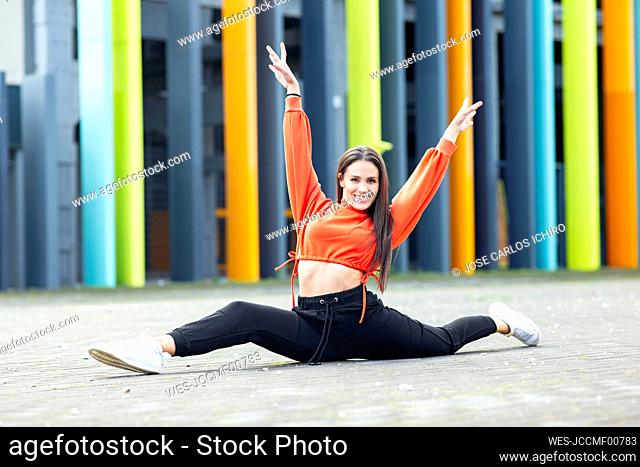 Portrait of beautiful brunette doing splits in front of colorful building