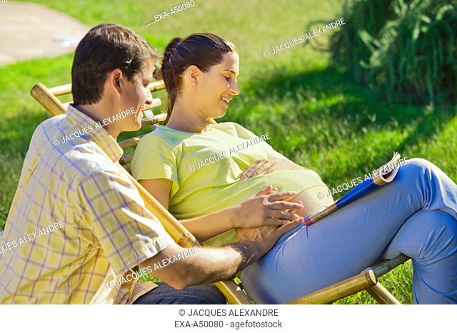 Husband touching his pregnant wifes belly on a warm summers day in the garden