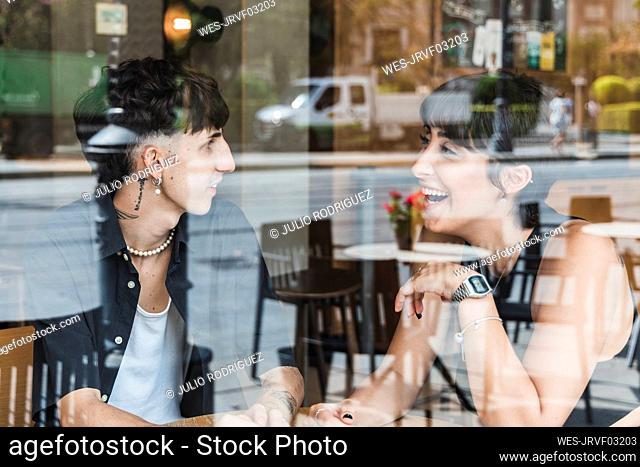 Happy young couple talking in cafe seen through glass