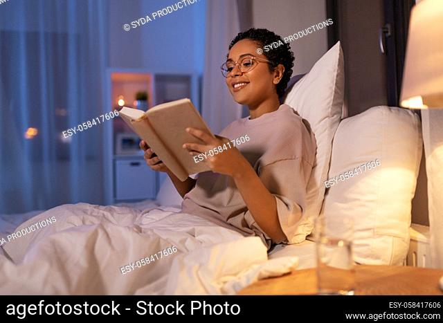 smiling young woman reading book in bed at home