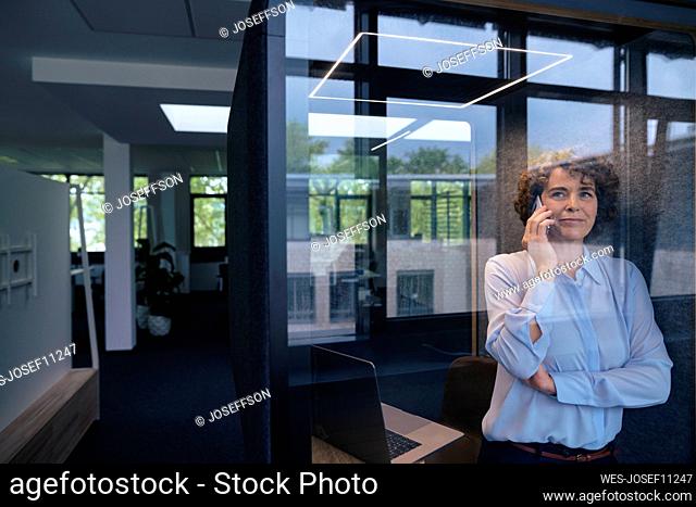 Smiling businesswoman talking through mobile phone in soundproof cabin