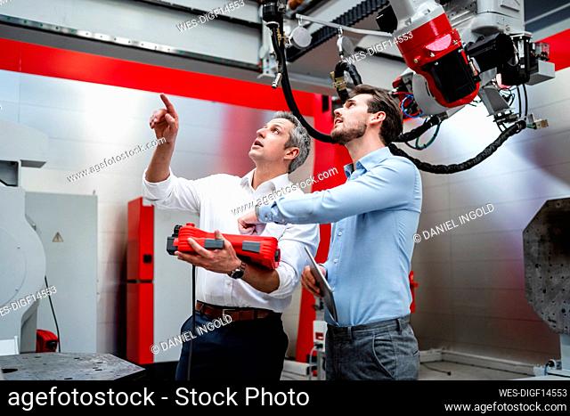 Male engineers examining robotics in factory