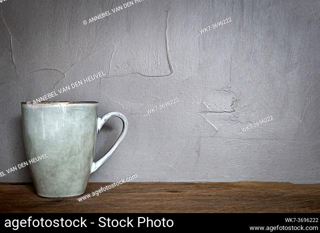 Ceramic mug with white foam gray natural stone design with concrete wall background, coffee or tea concept, copy space