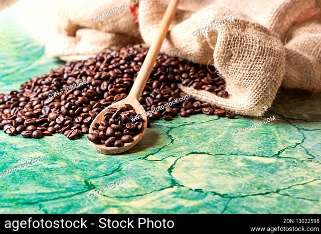 Coffee beans in coffee burlap bag on green surface and wooden spoon with coffee beans on top