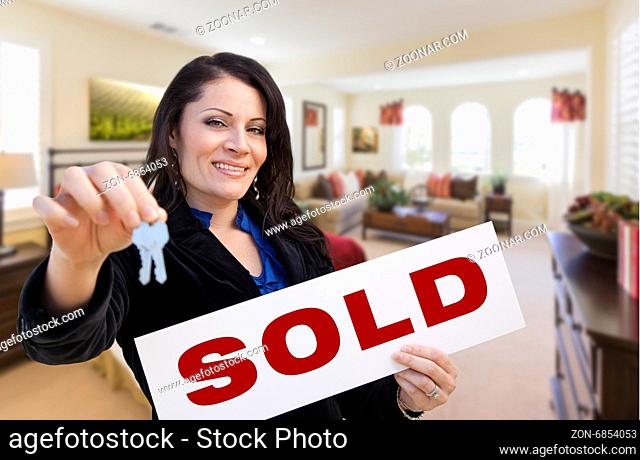 Happy Hispanic Woman with House Keys and Sold Sign in Beautiful Living Room