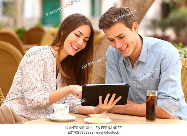 Happy couple watching media in a tablet in a restaurant terrace