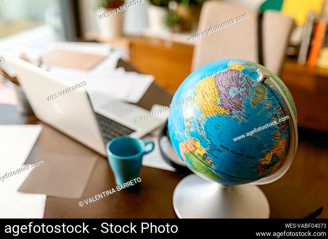 Globe with laptop and mug on table
