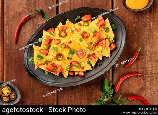 Nachos, Mexican tortilla chips, shot from above with a cheese sauce, chili and jalapeno peppers, tomatoes. and cilantro, on a dark rustic wooden background