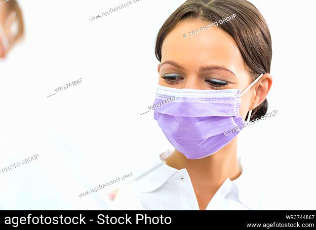 dentist in her practice or office treating male patient with assistant wearing mask