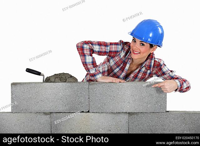 portrait of young female bricklayer pointing at concrete wall