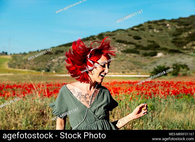 Cheerful woman tossing hair while dancing on poppy field