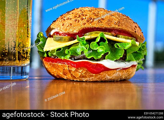 Delicious juicy burger and glass lager beer. Background of modern city. Bright sunny day. Vintage style