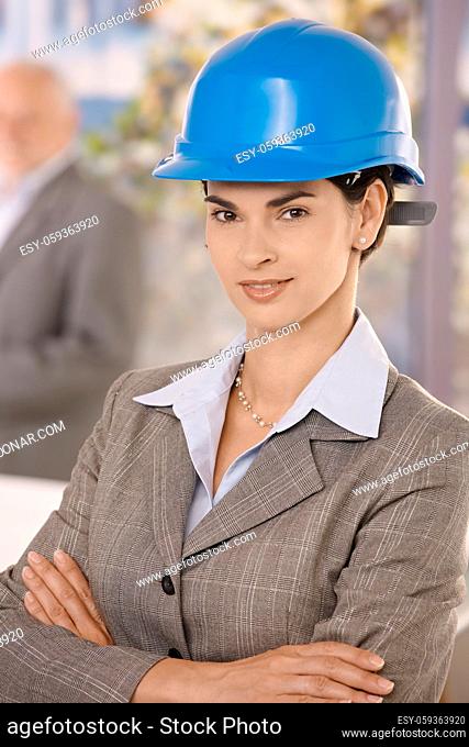 Portrait of businesswoman wearing hardhat, standing with arms crossed, smiling confidently at camera