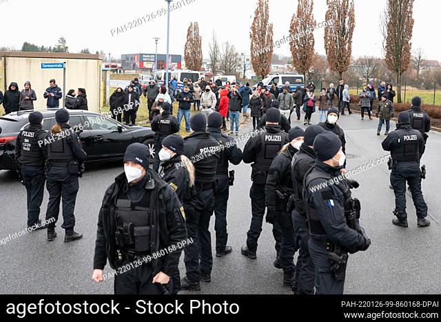 26 January 2022, Saxony, Bischofswerda: Demonstrators stand behind police officers on the sidelines of a visit by Saxony's Prime Minister Kretschmer to the...