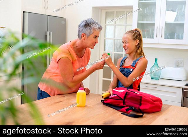 Senior grandmother giving granddaughter packed lunch and lollipop in kitchen
