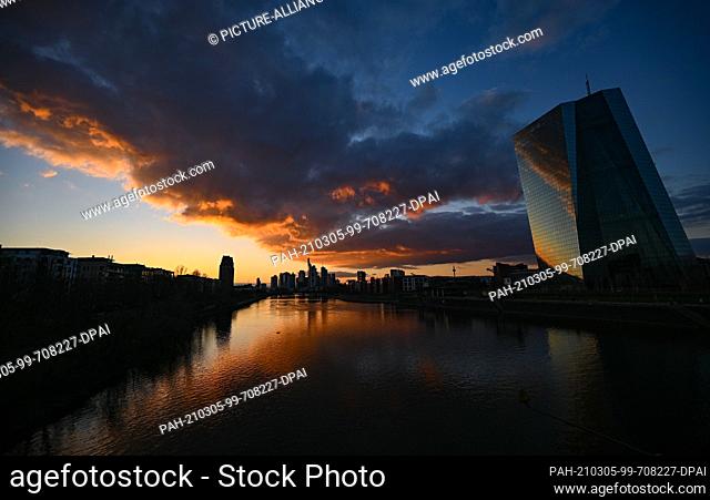 05 March 2021, Hessen, Frankfurt/Main: A colourful spectacle appears in the cloudy sky above the Frankfurt skyline and the ECB (r) at sunset