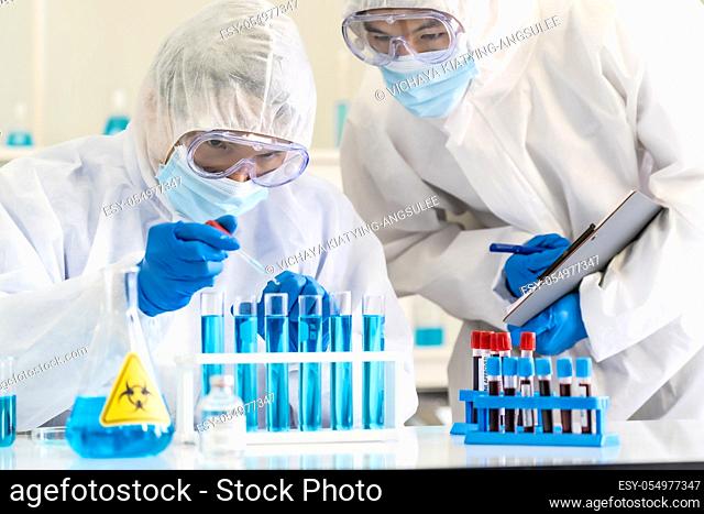 Scientists use dropper to drop chemical reagent to test tube in tube rack to research and develop vaccine for coronavirus covid-19 pandemic with his colleague