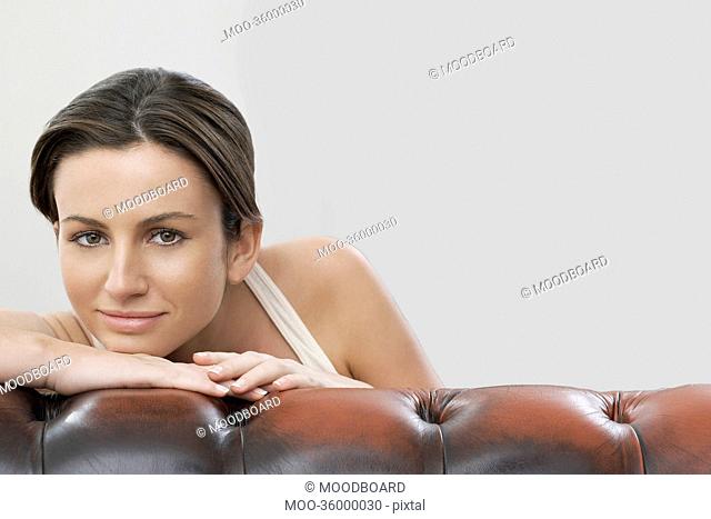 Portrait of beautiful woman on sofa against gray background