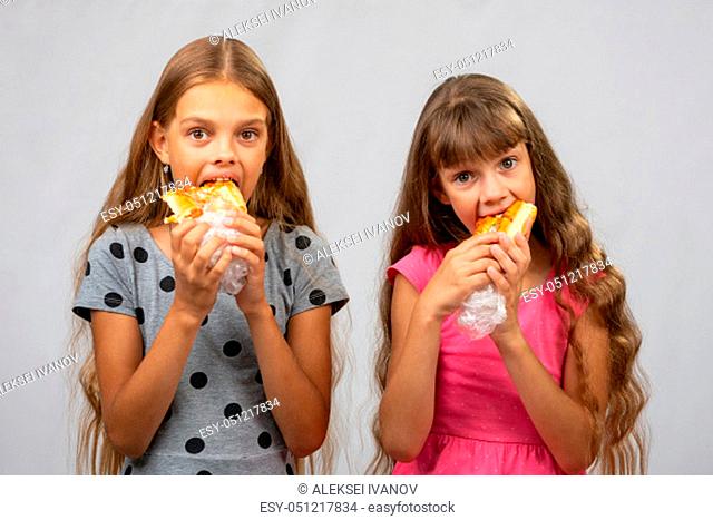 Two hungry girls eat bread, and look at the frame