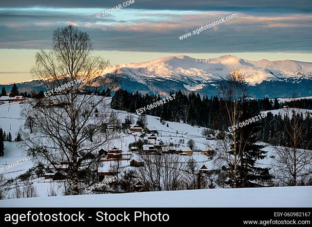 Small alpine village and winter snowy mountains in first sunrise sunlight around, Voronenko, Carpathian, Ukraine