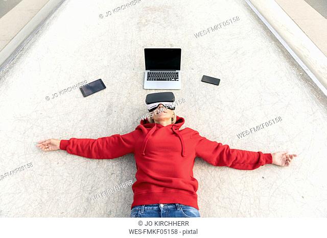 Senior woman lying on the ground wearing VR glasses next to mobile devices