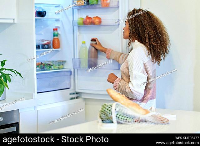 Afro young woman placing groceries into refrigerator at home