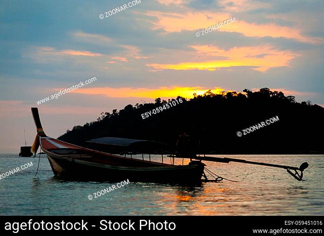 A longtail boat floating off the coast of Ko Lipe Island under a colorful sunset sky and setting sun in southern Thailand