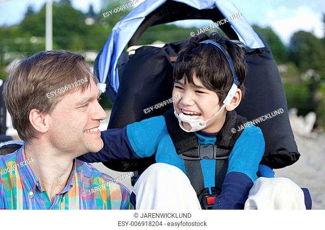 Father and disabled five year old son laughing together on beach
