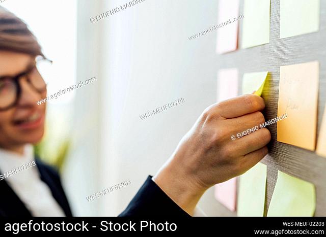 Businesswoman sticking adhesive note on wall in office